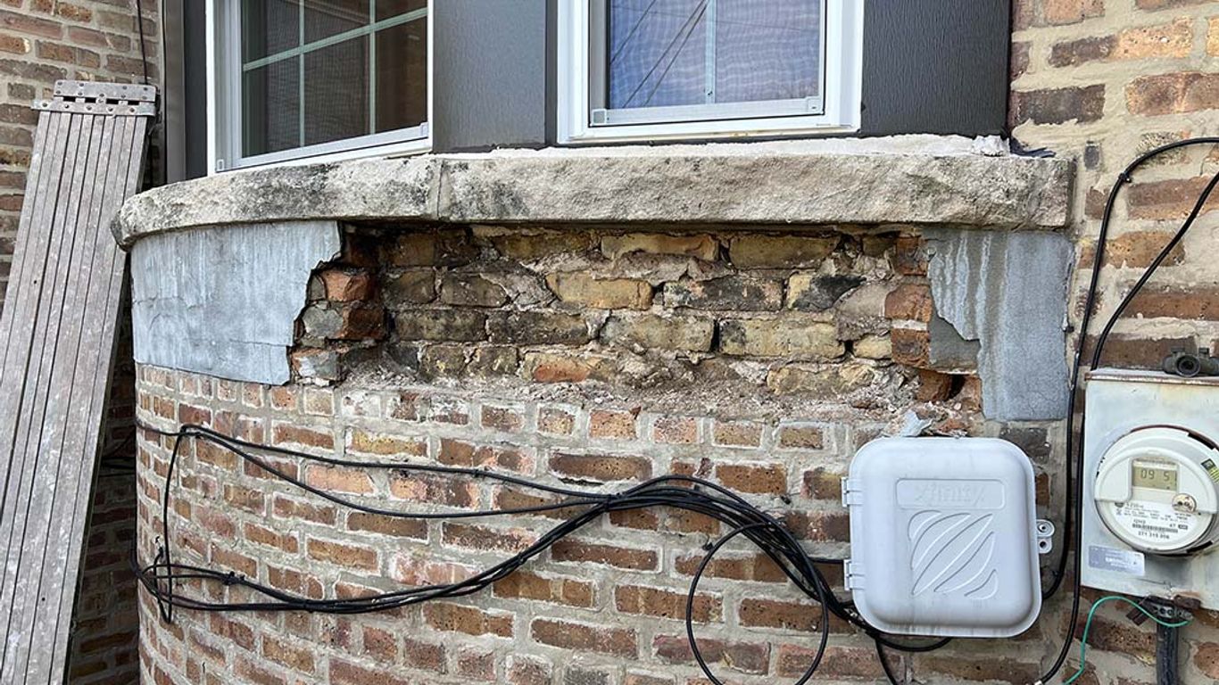 Damaged brickwork below a window with exposed wires and utility boxes.