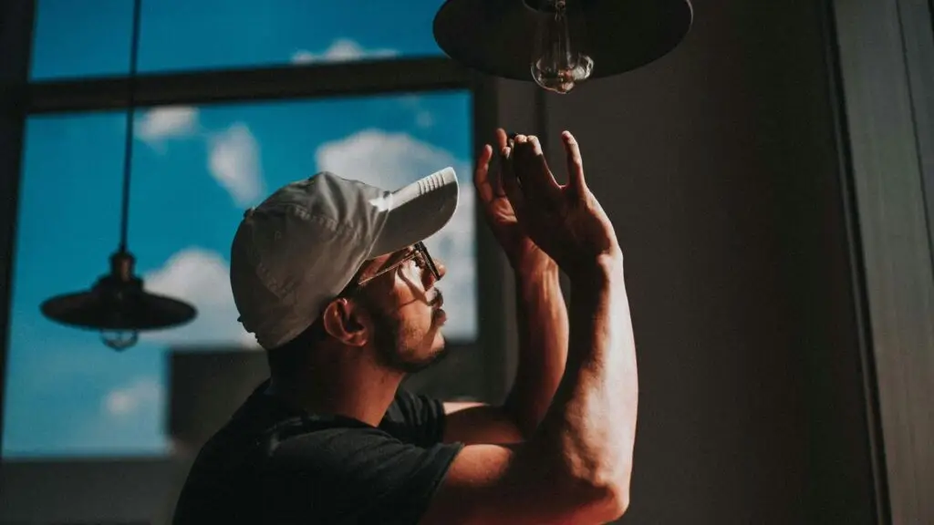 Commercial electrician – man in black shirt wearing white cap holding clear glass lamp