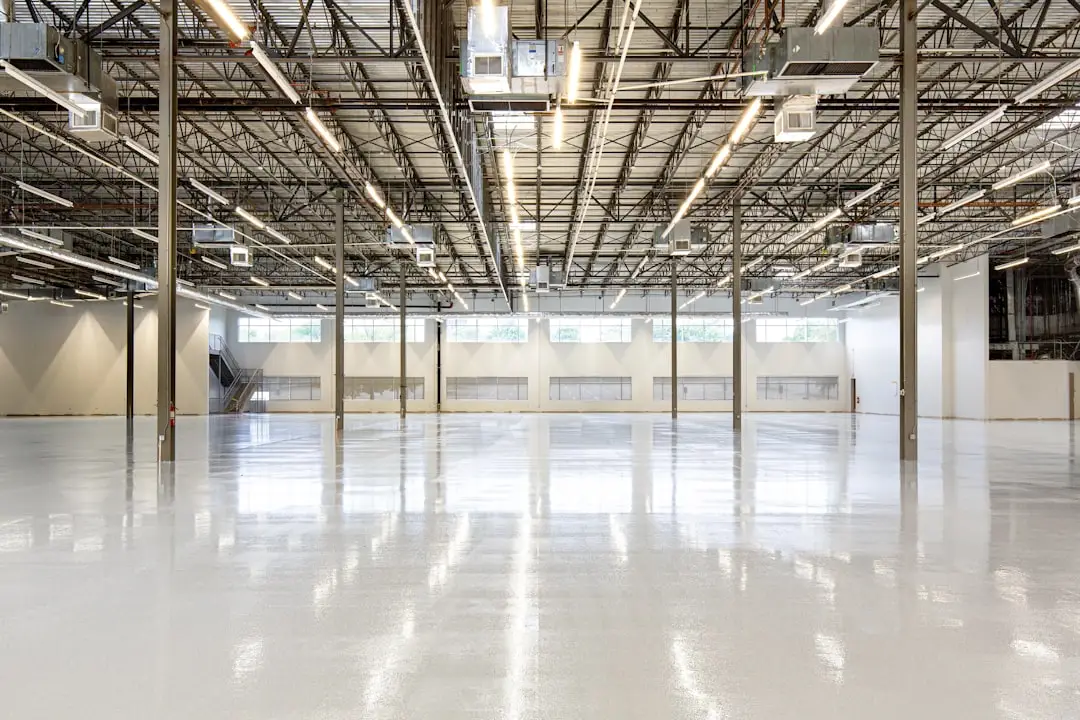 A large, empty industrial warehouse with shiny floors, high ceilings, exposed beams, and commercial wiring discreetly installed throughout the space. Several windows let in natural light.