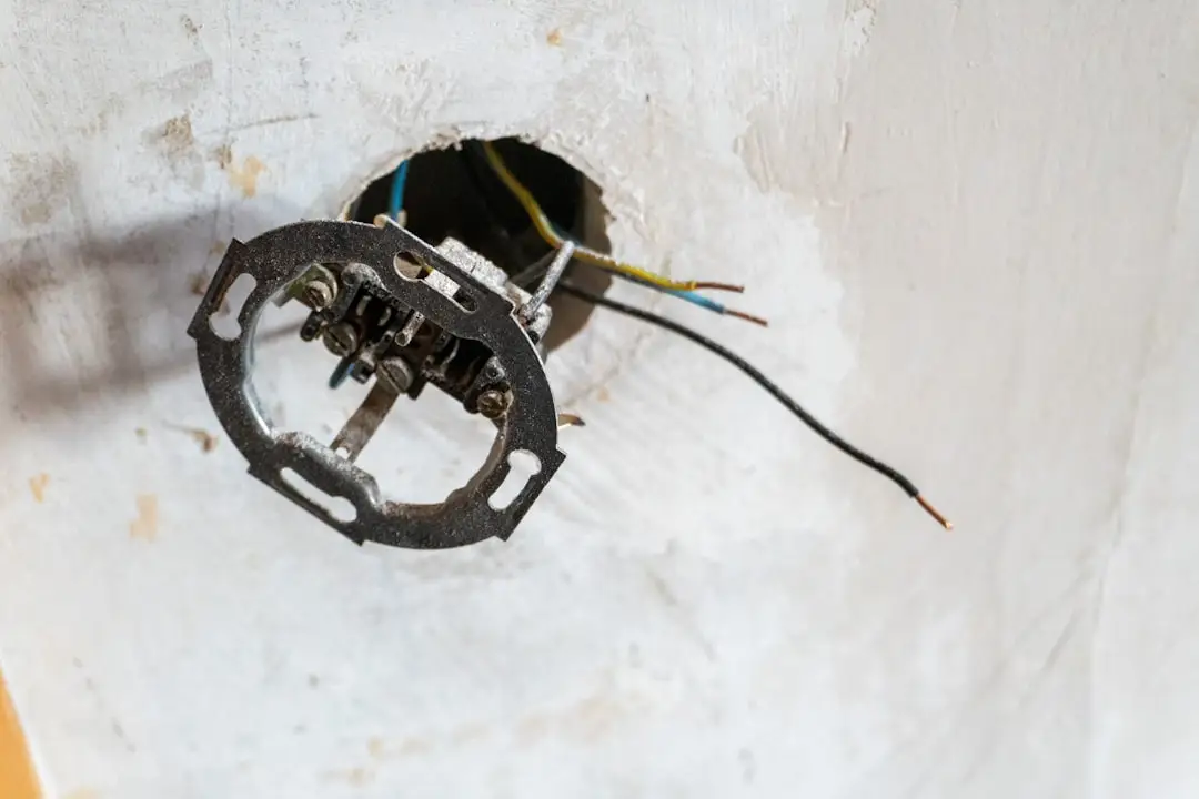 Exposed electrical wiring and a loose light fixture mounting bracket protruding from a hole in a white wall, indicating unfinished or ongoing electrical work—common signs encountered when diagnosing home electrical problems.