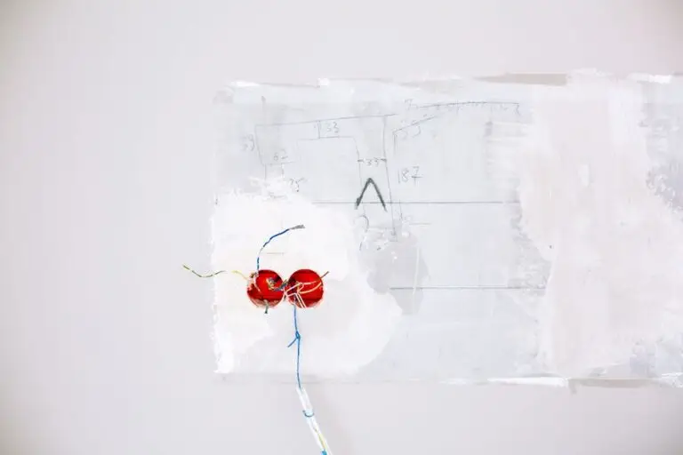 Exposed electrical wires and red wire nuts, indicative of residential wiring installation, protrude from a partially painted white wall. Faint pencil sketches and measurements are visible on the wall near the wiring.