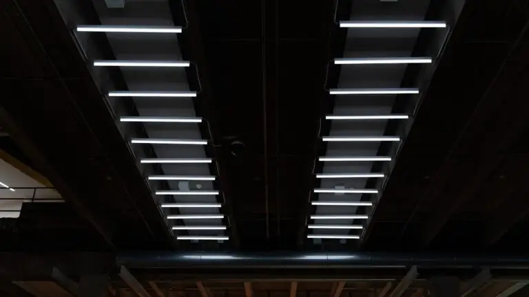 Two parallel rows of evenly spaced, horizontal retrofit fluorescent lighting LED fixtures are mounted on a dark industrial ceiling, creating a symmetrical pattern.