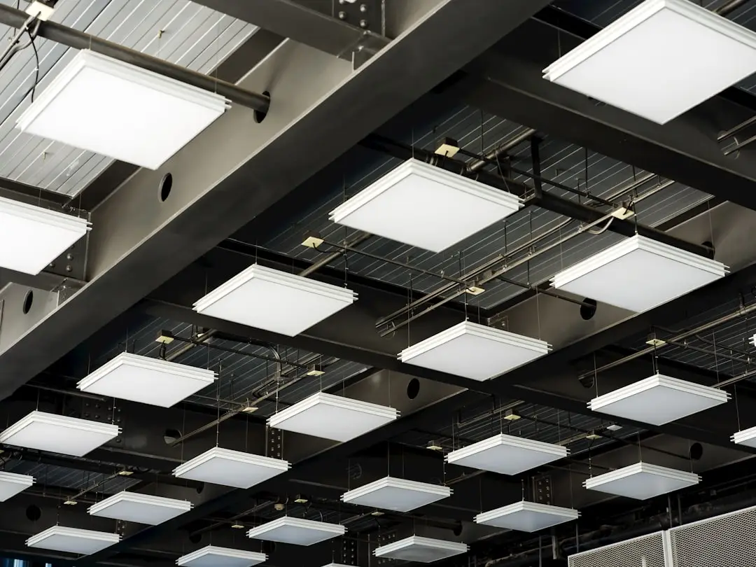 A ceiling with multiple square, white LED panel lights arranged in a grid pattern, suspended from metal beams—an energy-efficient setup that can significantly reduce lighting costs and shorten the LED retrofit payback period.